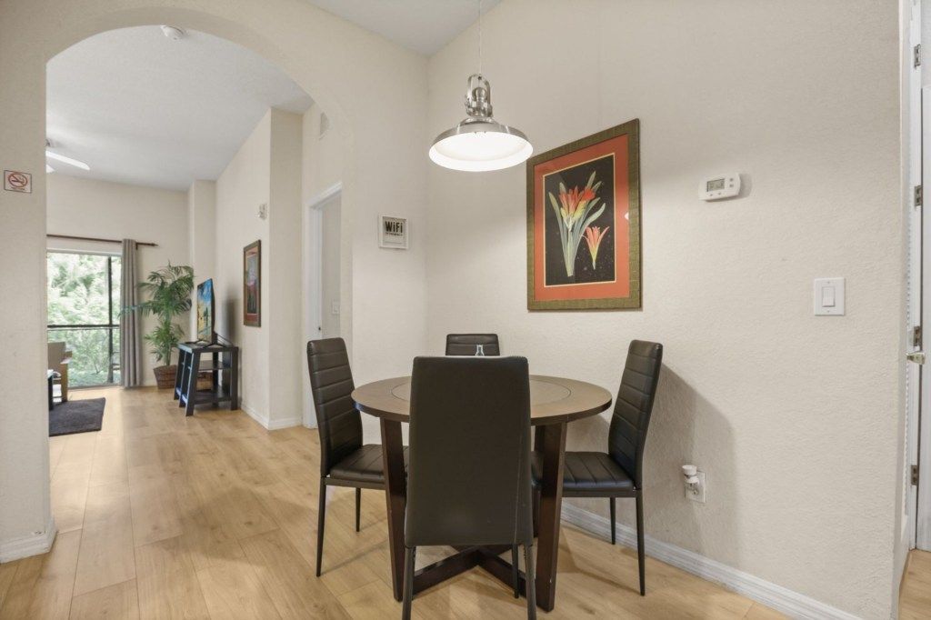 Un comedor con una mesa redonda y cuatro sillas, una lámpara colgante y un cuadro en la pared.