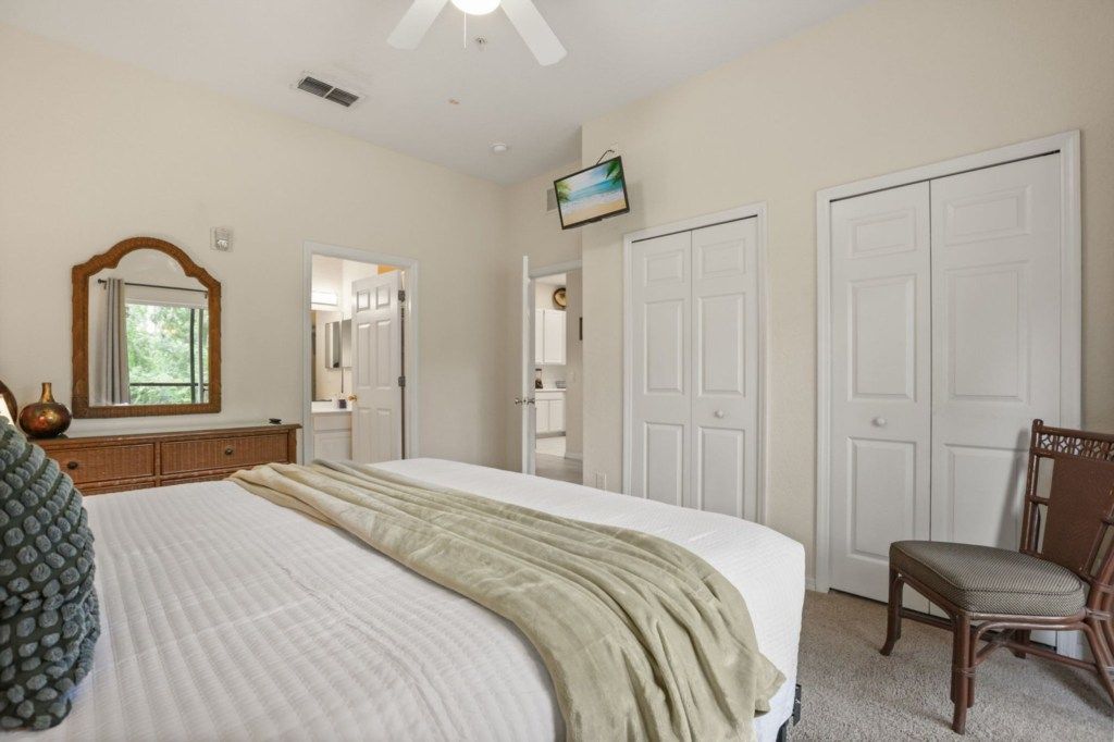 A bedroom with a bed, a chair, a dresser, a mirror, and two doors.