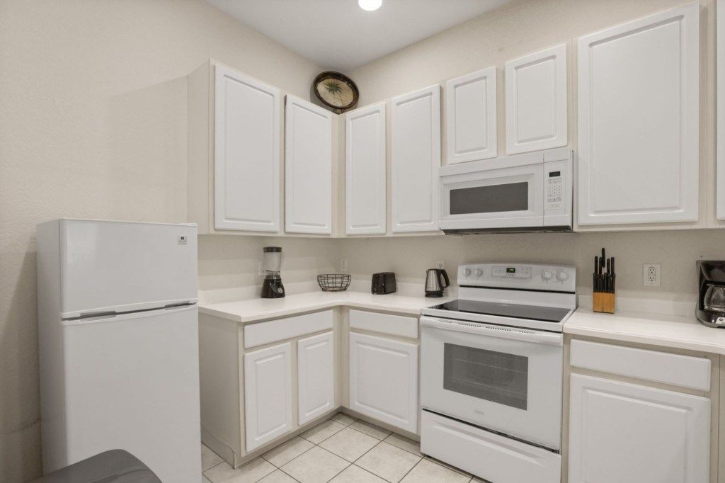 A kitchen with white cabinets, a refrigerator, a microwave, a stove, and a coffee maker.