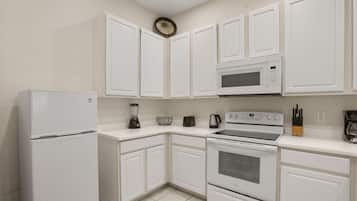 A kitchen with white cabinets, a refrigerator, a microwave, a stove, and a coffee maker.