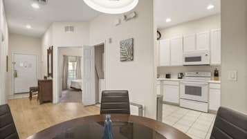 A modern kitchen with white cabinets, a microwave, and an oven. There is a dining area with a glass table and chairs.