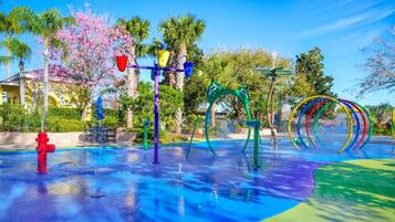 A water park with various play structures, including a red fire hydrant, a purple and yellow water feature, and a green arch.