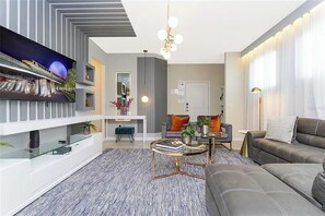 A modern living room with a sofa, coffee table, and TV. - 5 BD/ 5.5 BA/ Solterra (7256 OL) (Davenport)