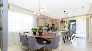 A modern kitchen with a dining area, featuring a central island, pendant lighting, and a view into the living space. - 5 BD/ 5.5 BA/ Solterra (7256 OL) (Davenport)