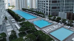 Ein Poolbereich auf dem Dach mit mehreren Pools und Liegestühlen, umgeben von Bäumen und Hochhäusern.