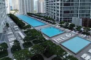 Ein Poolbereich auf dem Dach mit mehreren Pools und Liegestühlen, umgeben von Bäumen und Hochhäusern.