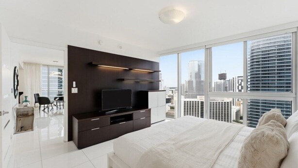 Ein modernes Schlafzimmer mit einem großen Bett, einem Fernseher und Blick auf die Stadt.