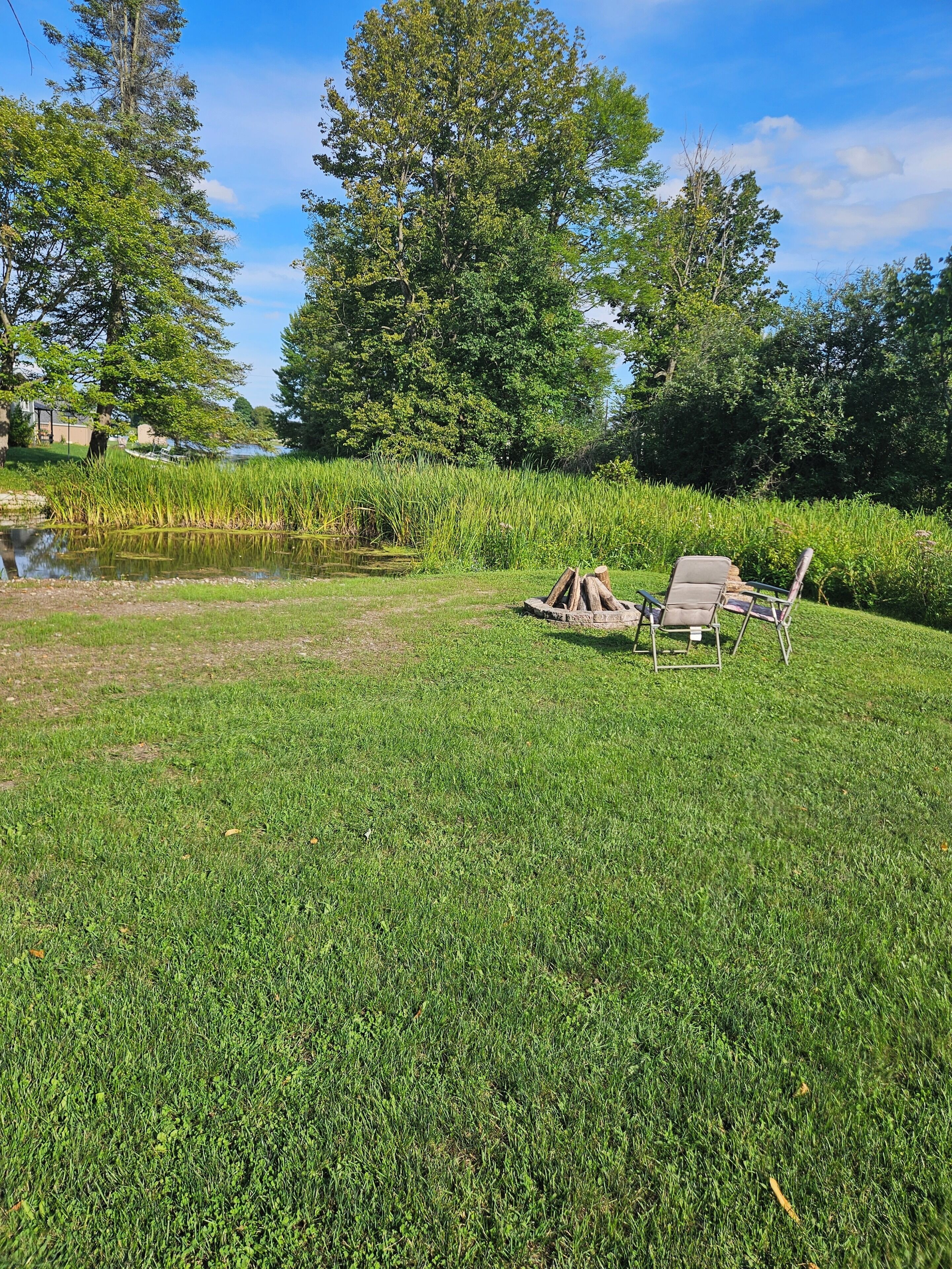 A grassy area with a pond, trees, and two chairs.