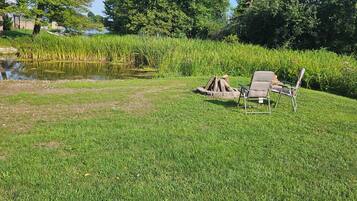 A grassy area with a pond, trees, and two chairs.