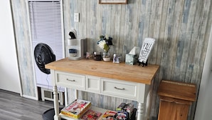 Une pièce avec un bureau en bois, une horloge, un cadre représentant une photo de famille, un ventilateur et une poubelle.