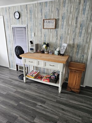 A room with a wooden desk, a clock, a framed family sign, a fan, and a trash bin.
