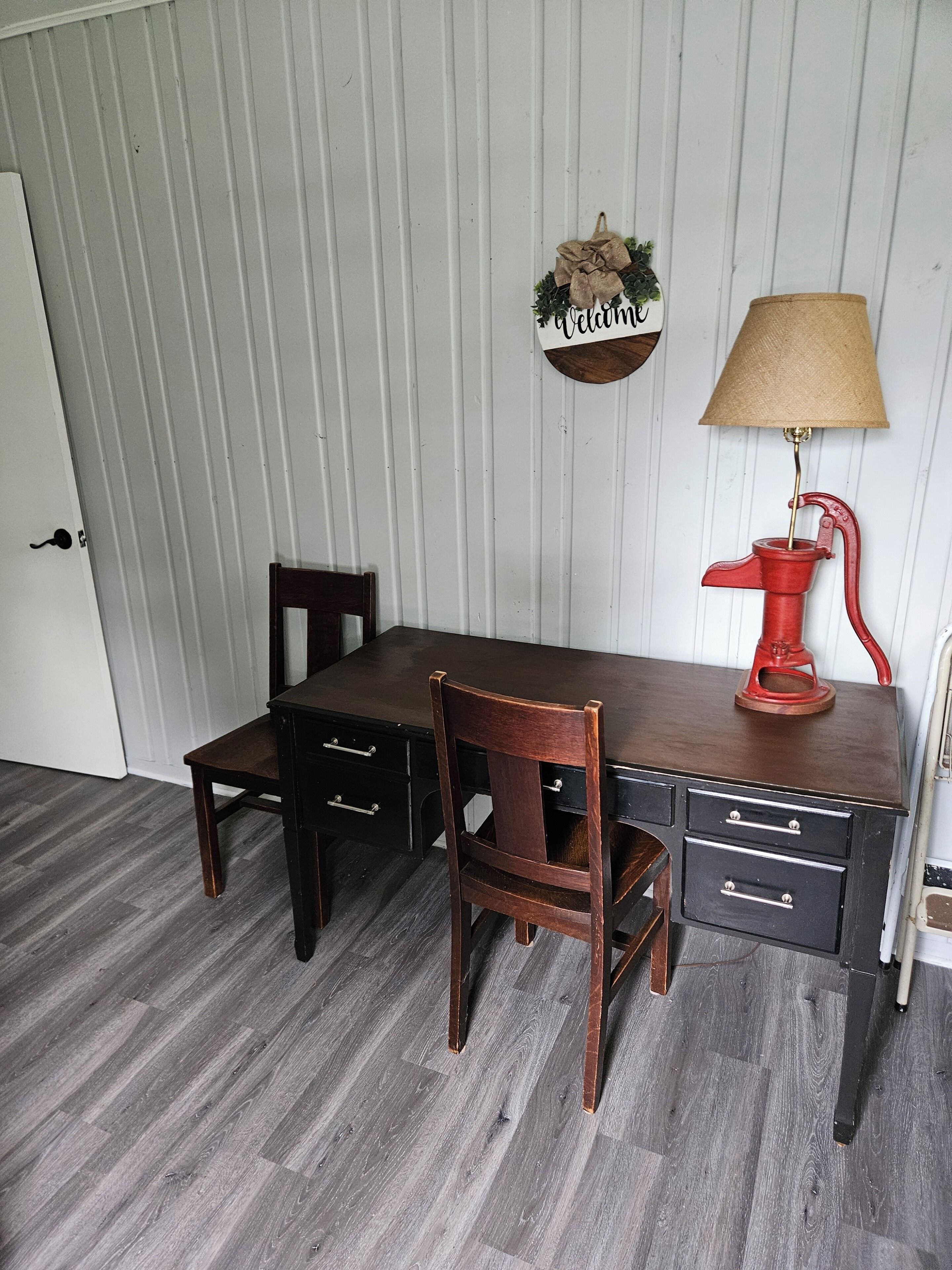 Un coin repas avec une table et des chaises en bois, une lampe rouge de style vintage et un panneau fixé au mur.