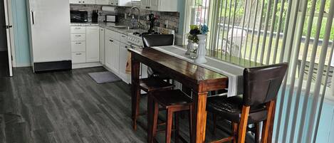 Una cucina con zona pranzo, mobili bianchi, un frigorifero, un fornello e una ventola a soffitto.