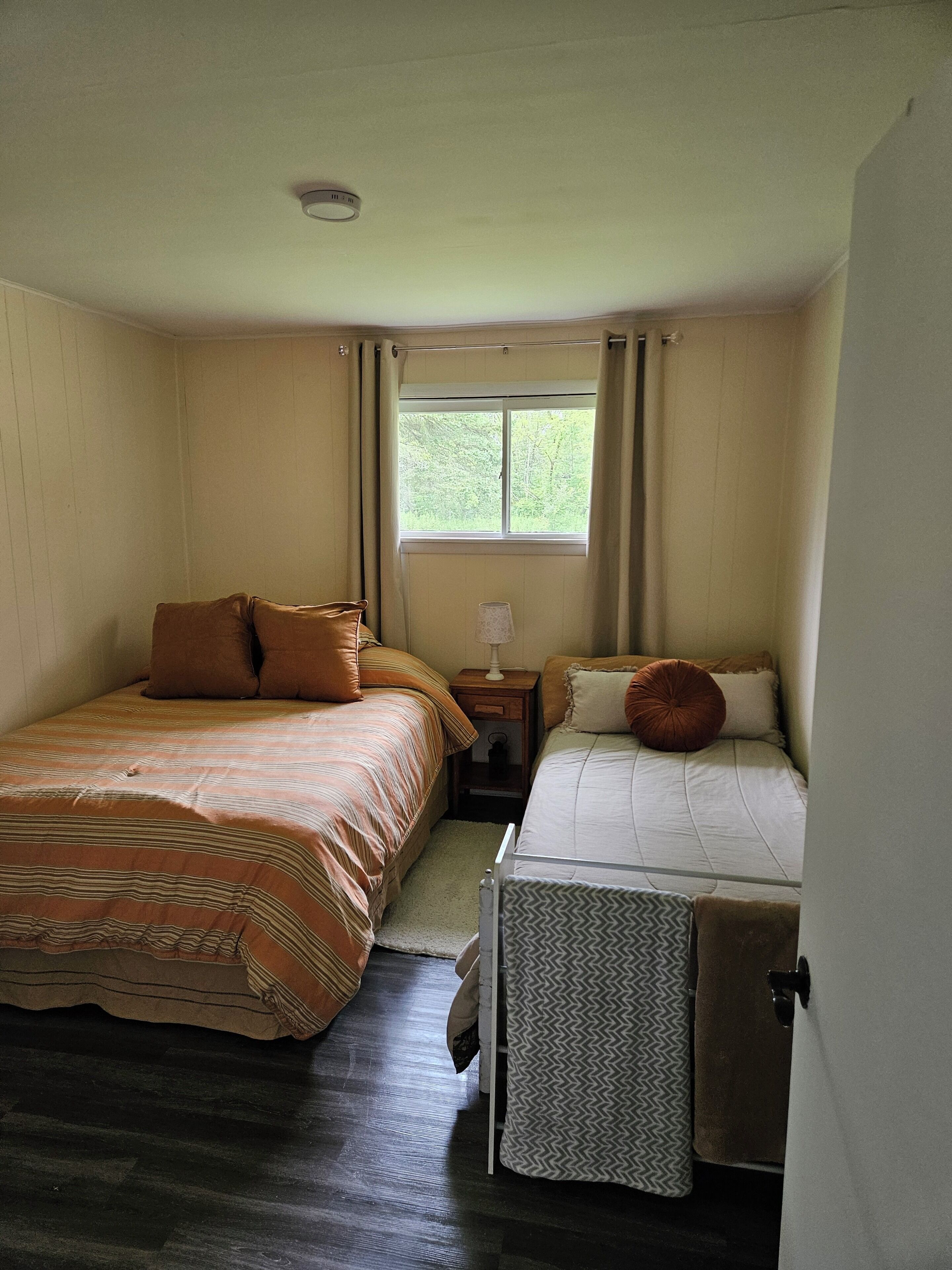 A bedroom with two beds, a window, a nightstand, and a lamp.