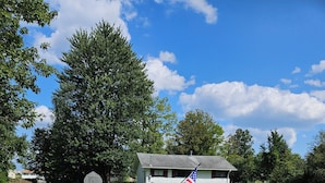 Un chemin de gravier mène à un bâtiment blanc surmonté d’un mât et arborant le drapeau américain.