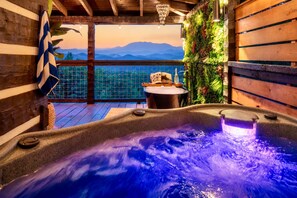 Uma banheira de hidromassagem com vista para as montanhas, um deck de madeira e uma mesa com um livro.
