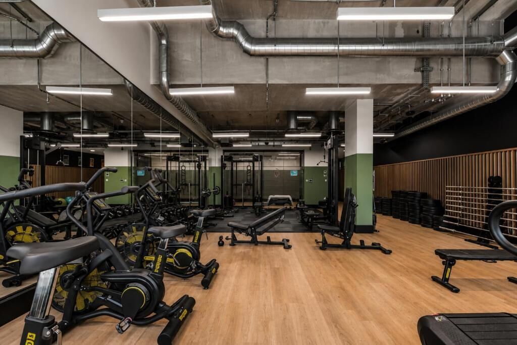 A gym with various exercise equipment, including treadmills and weight machines, and a wooden floor.
