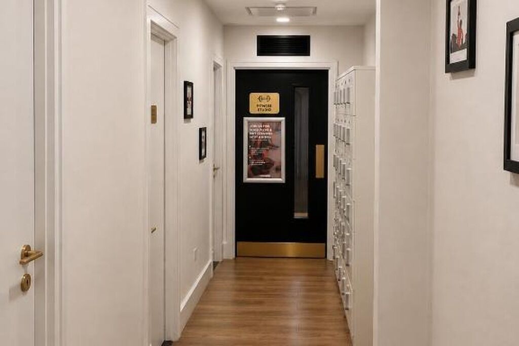 A hallway with a black door at the end, a poster on the wall, and a series of framed pictures on the right.