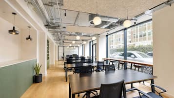 Un salón de conferencias moderno con mesas y sillas, ventanas amplias y conductos visibles en el techo.