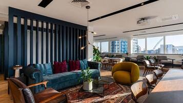 A modern office space with a blue and black color scheme, a sofa, a yellow chair, a conference table, and large windows offering a city view.