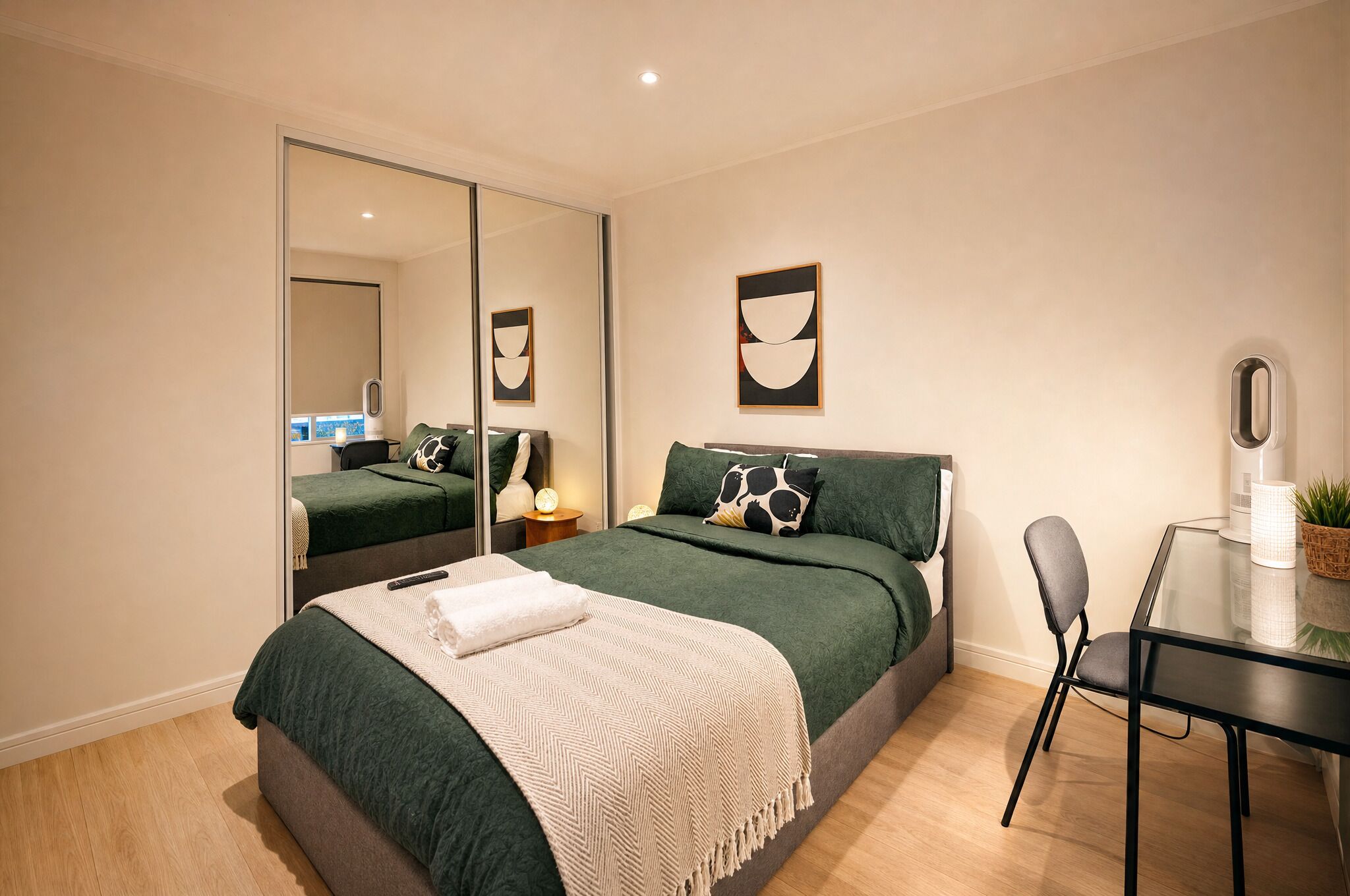 A modern bedroom with a bed, a desk, and a mirror.