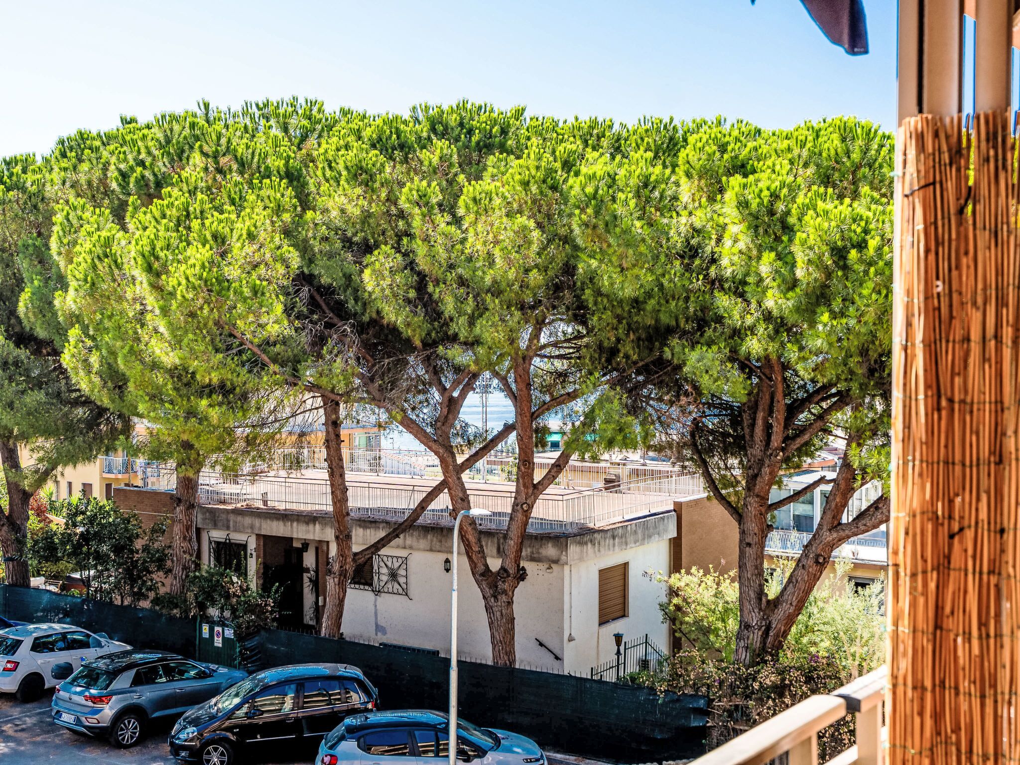 A parking area with cars, a building with a balcony, and trees.