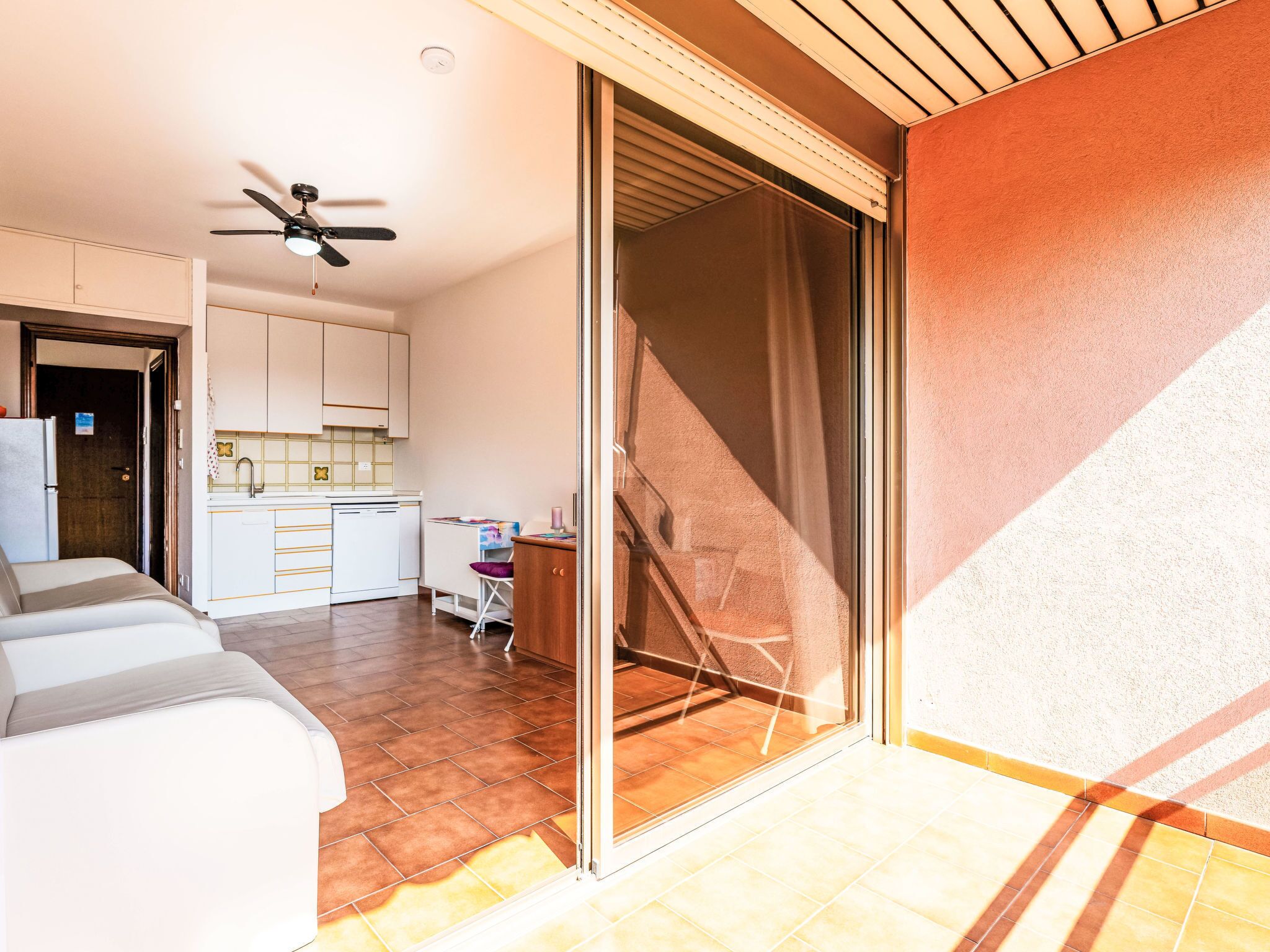 Una cocina moderna con armarios blancos, ventilador de techo y puerta corrediza de vidrio que da a un espacio exterior.
