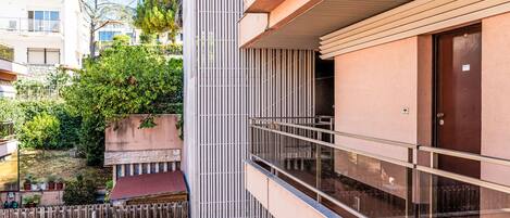A modern building with a balcony, a wooden door, and a view of the surrounding area including trees and other buildings.