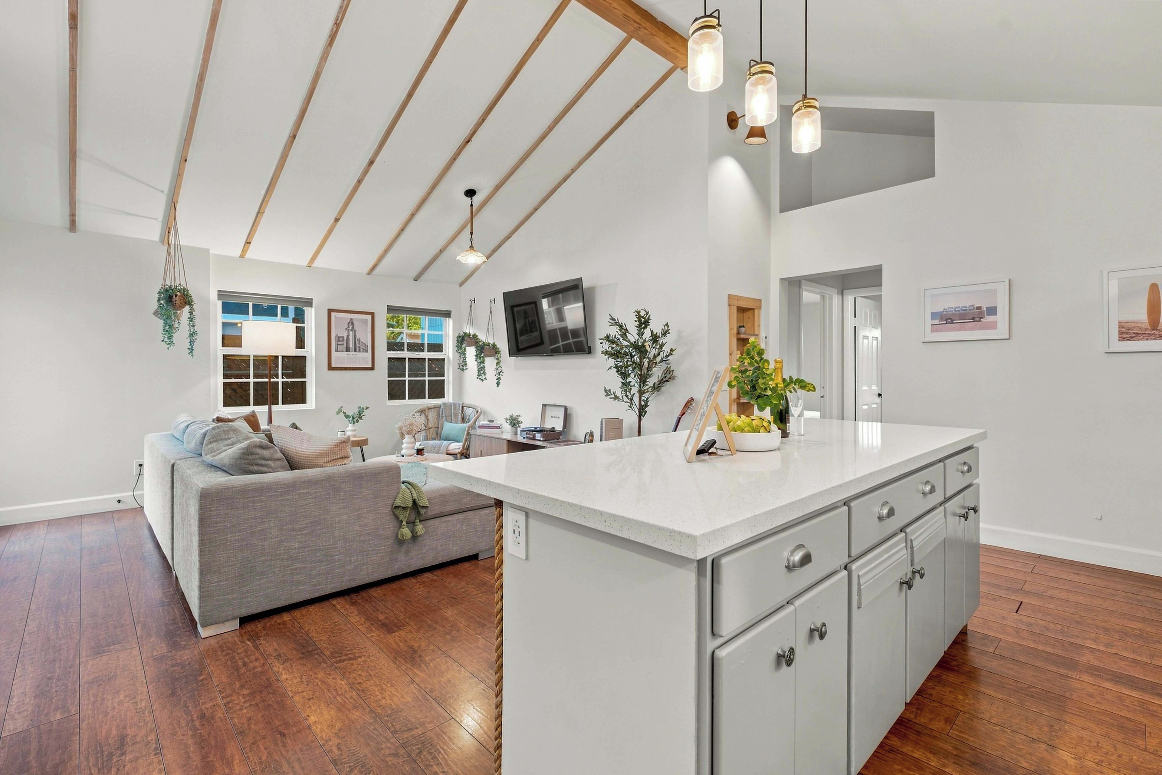 A spacious living area with a large island, wooden flooring, and a high ceiling with exposed beams.