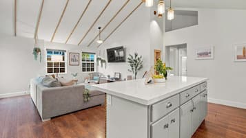 A spacious living area with a large island, wooden flooring, and a high ceiling with exposed beams.