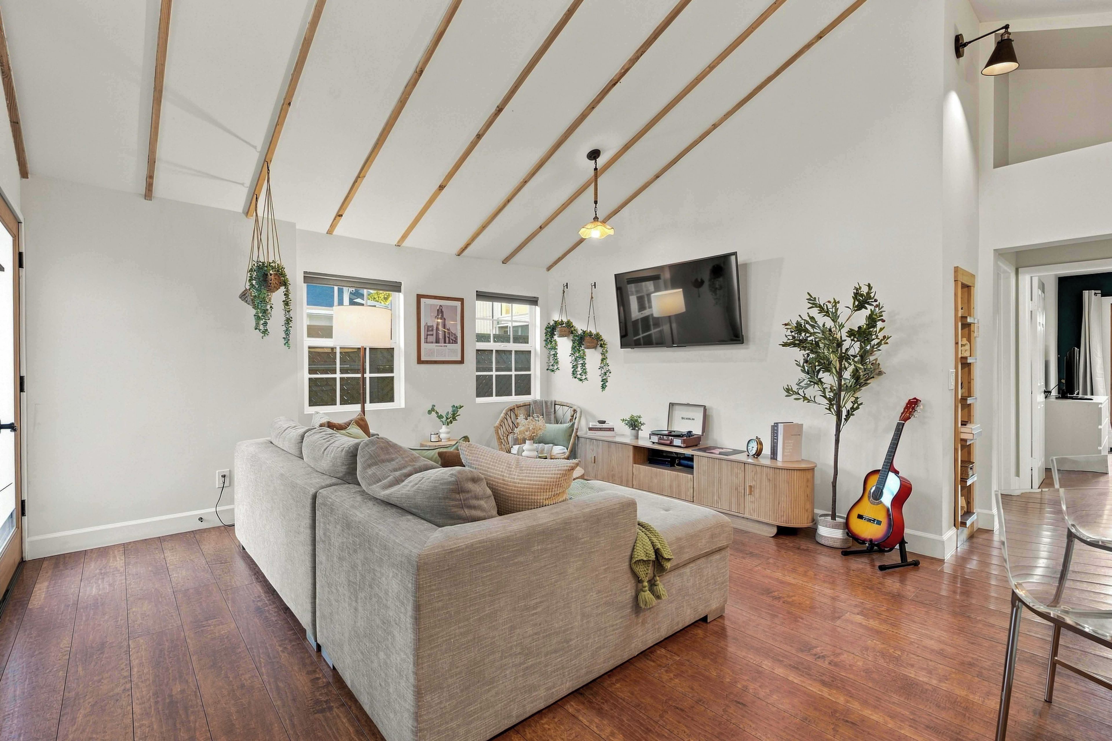 Ein modernes Wohnzimmer mit einer Couch, Holzboden, einem Fernseher und einer Gitarre.