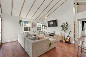 Een moderne woonkamer met een bank, houten vloeren, een televisie en een gitaar.