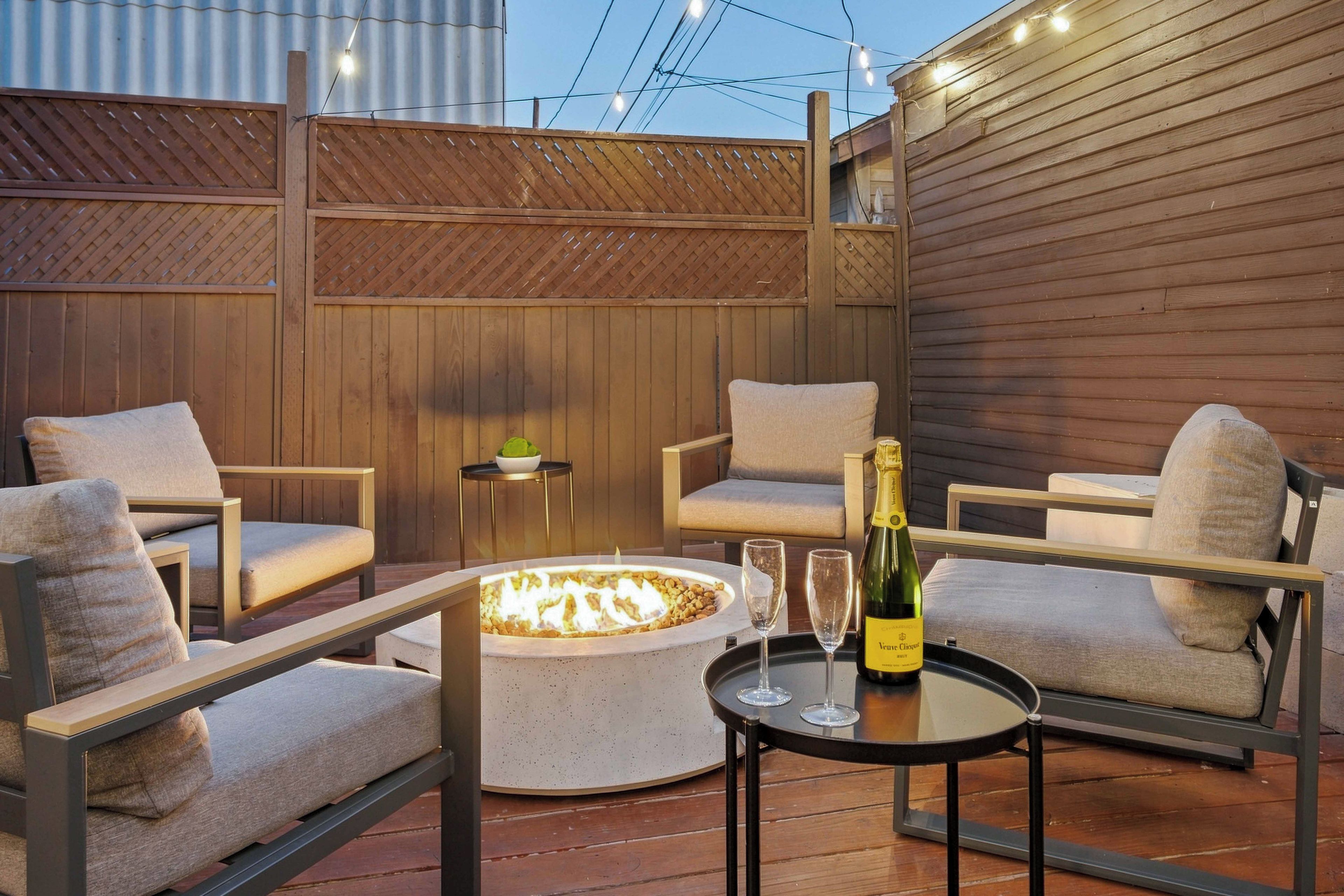 Une terrasse avec un foyer, des sièges et une bouteille de champagne.