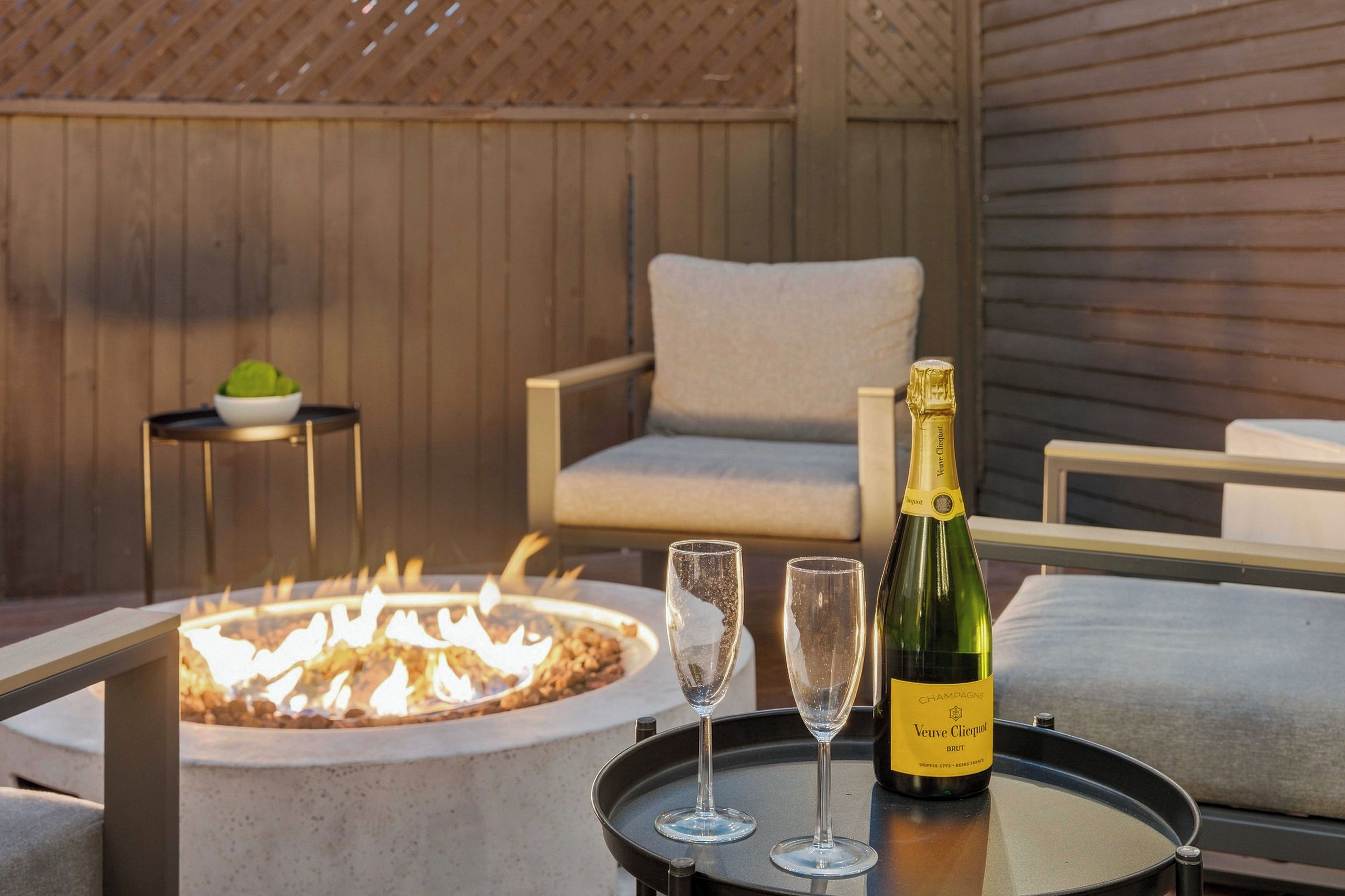 A fire pit with two glasses and a bottle of Veuve Clicquot champagne on a tray.