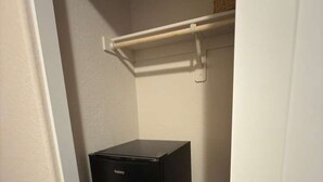 Un refrigerador negro compacto en un rincón de una habitación con una pared blanca y un estante de madera encima.
