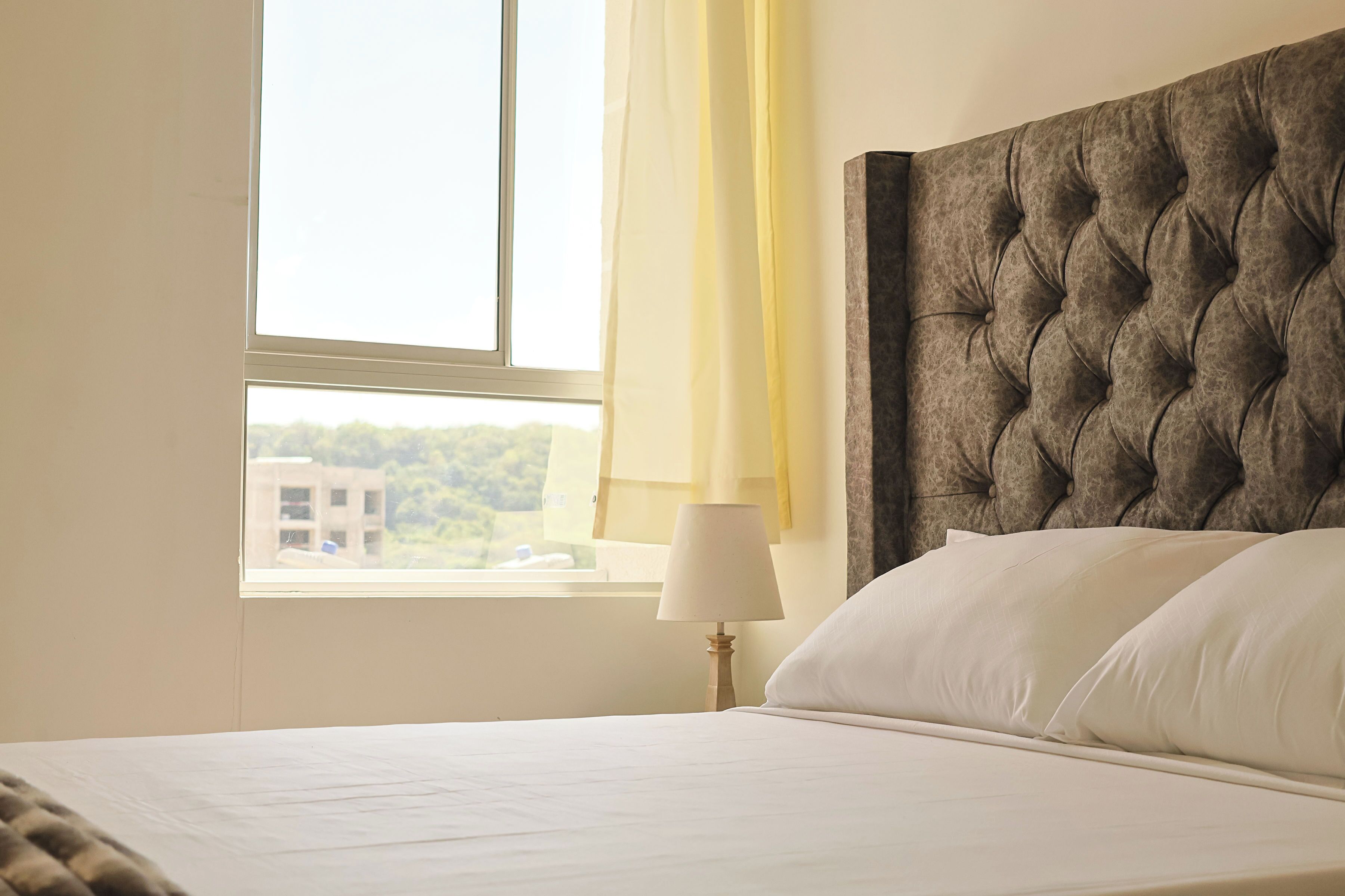 A hotel room with a large bed, a window with curtains, and a view of buildings outside.