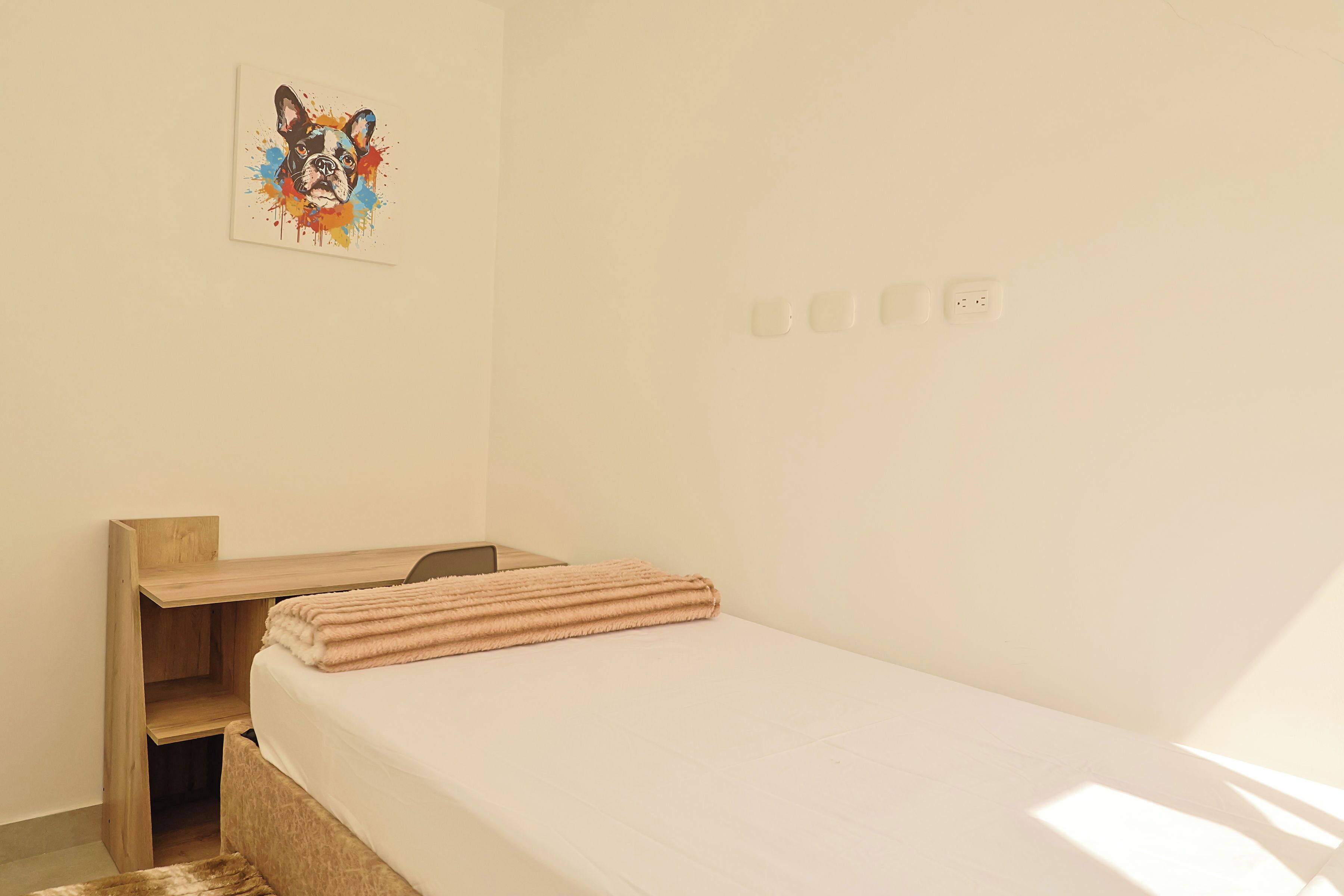 Ein schlichtes Zimmer mit einem Bett, einem Schreibtisch und einer Wandsteckdose.