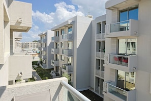 Un edifici residencial modern, de diverses plantes, amb balcons, una zona de piscina i un cel clar.
