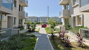 Um prédio residencial com varandas numeradas, um caminho pavimentado e um carro vermelho estacionado na entrada.