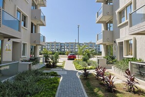 Un edificio residencial con balcones numerados, un camino pavimentado y un automóvil rojo estacionado en la entrada.
