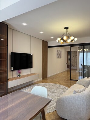 A modern living room with a flat-screen TV, a dining table, a sofa, and a patterned rug.