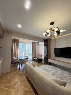 Een moderne hotelkamer met een bank, een eettafel met stoelen, een televisie en een plafondlamp.