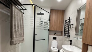 Moderni kylpyhuone, jossa on lasinen suihkuseinä, wc-istuin, pesuallas ja peili.