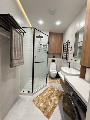 Ein modernes Badezimmer mit Duschkabine aus Glas, Toilette, Waschbecken und Spiegel.