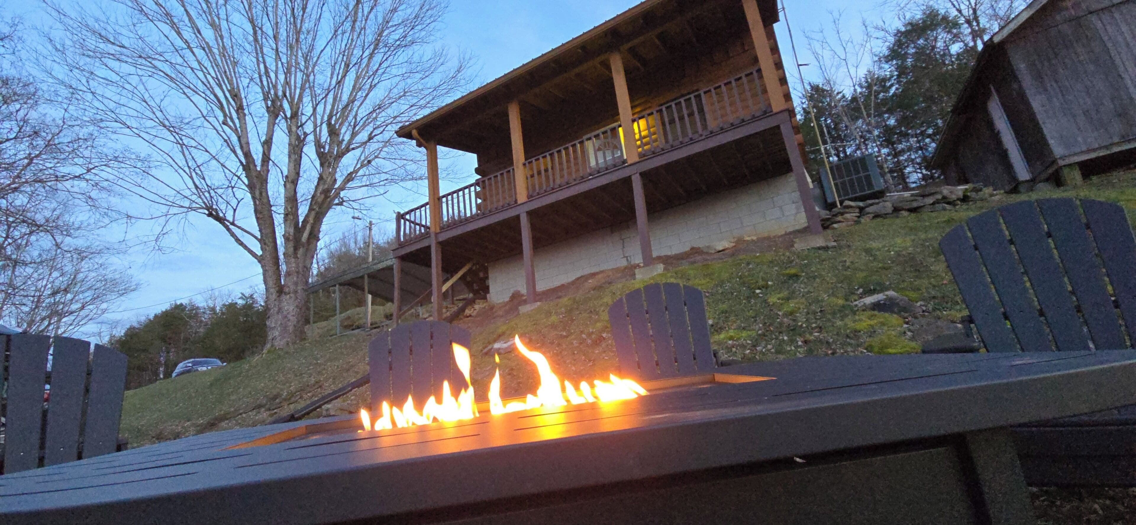 A deck with a fire feature, a covered outdoor area with a balcony, and a hillside backdrop.