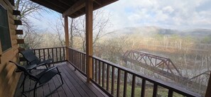 Eine Holzterrasse mit zwei Stühlen, mit Blick auf einen Fluss und eine Brücke.