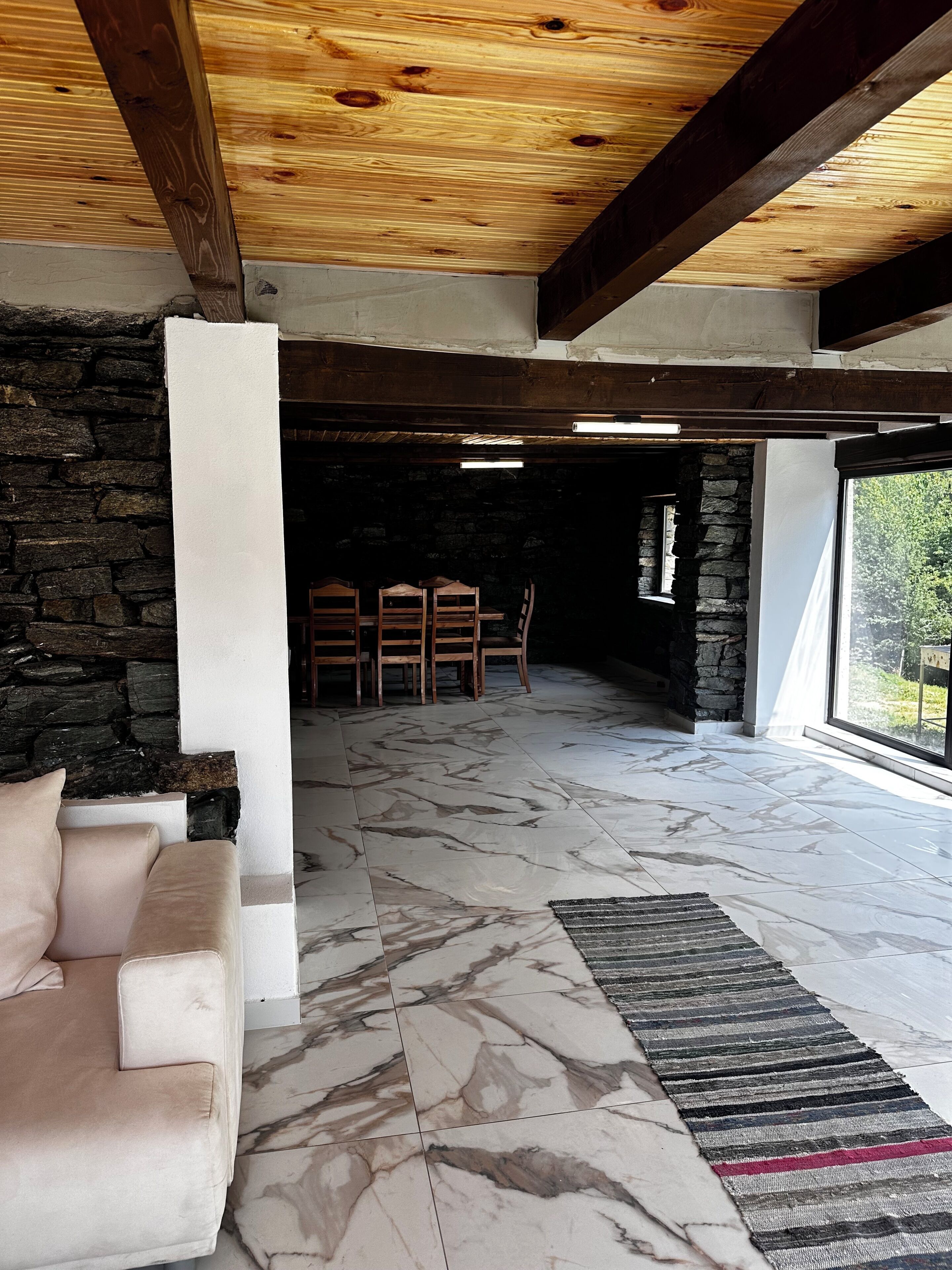 Un interior moderno con una pared de piedra, techo de madera y vistas amplias a través de un ventanal.