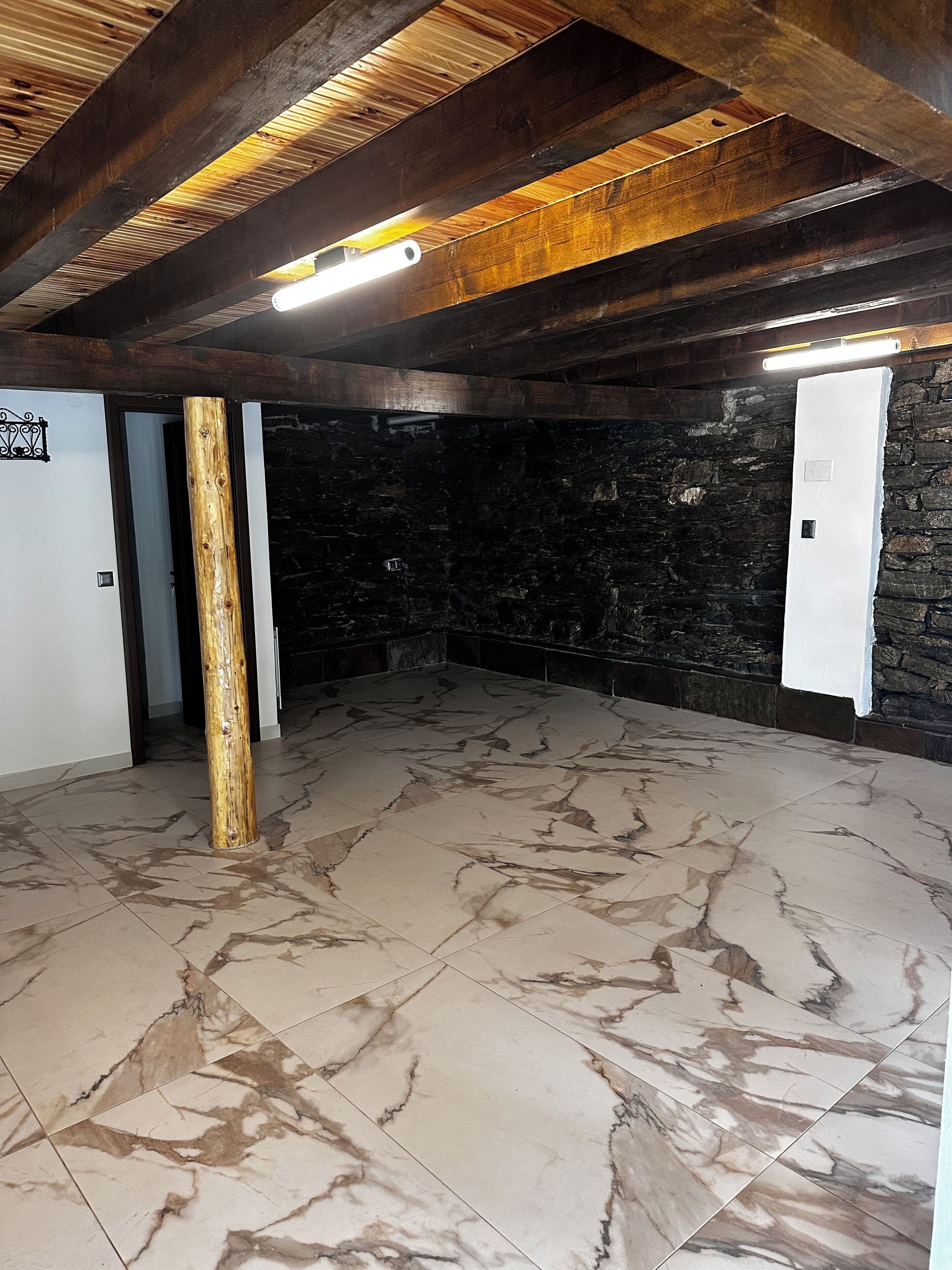 Une pièce avec un mur en pierre, un plafond avec des poutres en bois et un sol en marbre.