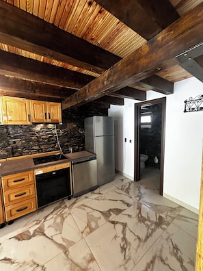 Una cocina con gabinetes de madera, protector contra salpicaduras de piedra, refrigerador de acero inoxidable y piso de baldosas de mármol.
