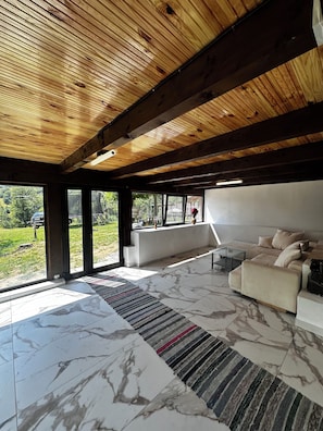 A spacious living area with a wooden ceiling, large windows, a beige sofa, and a marble floor. - House of the SoulCharming 12-bedroom chalet  in Avram Iancu (Avram Iancu)